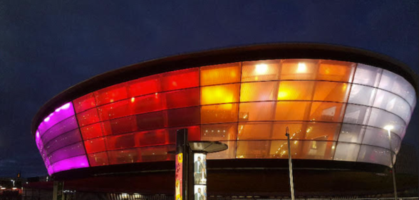 A photo showing the OVO Hydro Arena in Glasgow illuminated in lesbian Pride flag colours