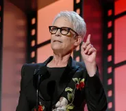 A photo of actor Jamie Lee Curtis wearing glasses and a black dress on stage at the AARP awards in LA.