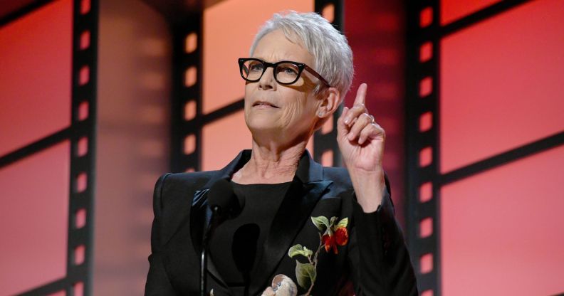 A photo of actor Jamie Lee Curtis wearing glasses and a black dress on stage at the AARP awards in LA.