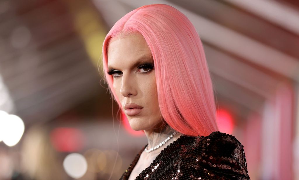 Jeffree Star looks at the camera wearing a pink straight wig, dark top and white necklace.