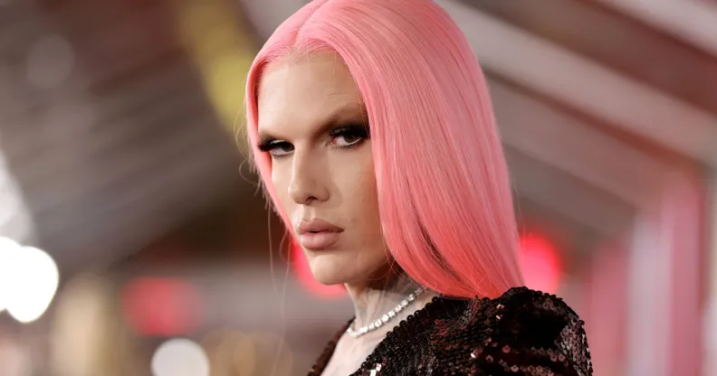 Jeffree Star looks at the camera wearing a pink straight wig, dark top and white necklace.