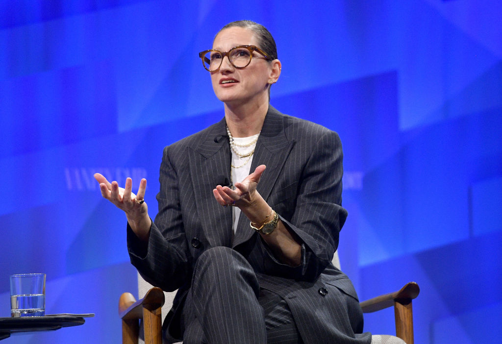 Jenna Lyons is sitting in a suit mid sentence speaking at a panel.