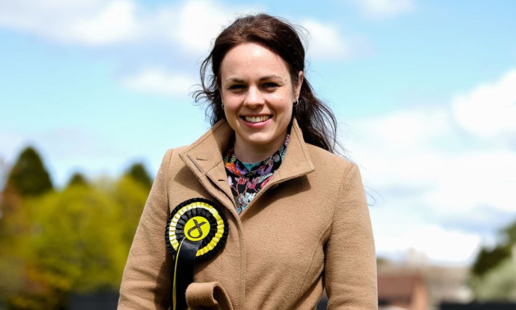 Kate Forbes, one of the SNP leadership hopefuls, pictured on the campaign trail wearing an SNP badge in an outdoor location. Trees can be seen in the background.