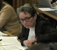 A screenshot of Labour MP Kate Osbourne wearing a white shirt and black suit jacket as she sits at a desk with papers in front of her during a women and equalities committee meeting
