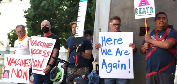 The LGBTQ+ community comes together for a protest about monkeypox. People hold signs that say "here we are again" and imploring the government to get more vaccines.