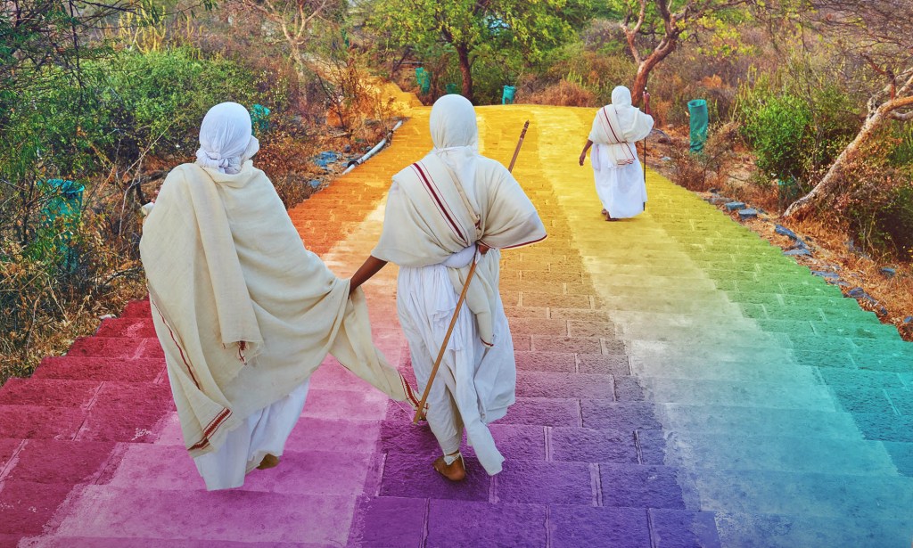 Jains wearing white robes walk down steps coloured in the LGBT Pride flag