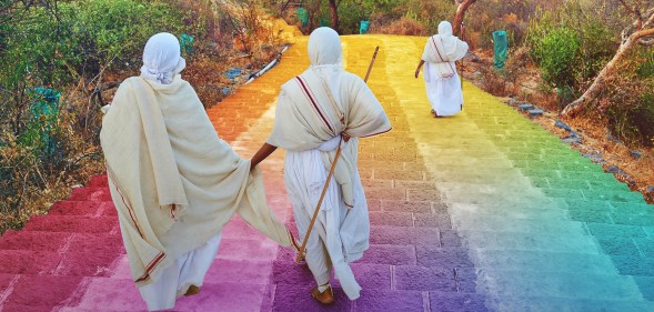 Jains wearing white robes walk down steps coloured in the LGBT Pride flag