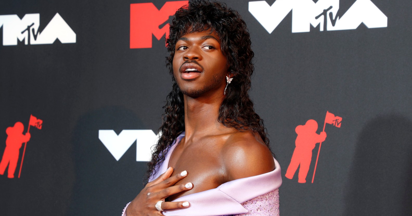 Lil Nas X wears a long black wig and off-the-shoulder lilac dress at the MTV VMAs 2021