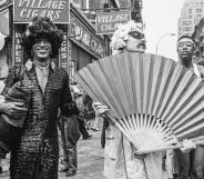 Marsha P Johnson pictured at a march in the early '70s. She is pictured wearing a long dress and a hat besides two activists who are holding up a giant fan. They are pictured on the streets of New York.