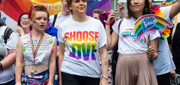 Nicola Sturgeon at the 2018 Pride Festival in Glasgow. She is pictured wearing a t-shirt that reads "Choose Love" in rainbow colours. Queer activists are pictured either side of her and in the background is a rainbow banner.