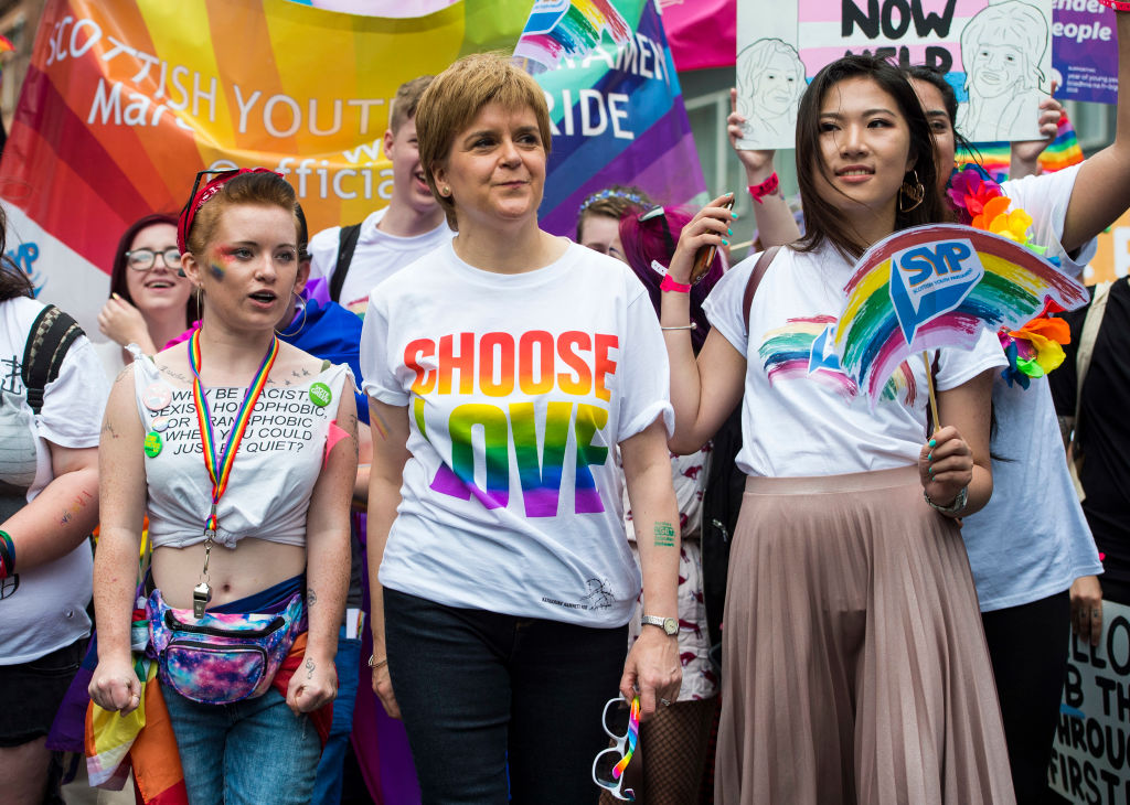 Nicola Sturgeon at the 2018 Pride Festival in Glasgow. She is pictured wearing a t-shirt that reads "Choose Love" in rainbow colours. Queer activists are pictured either side of her and in the background is a rainbow banner.