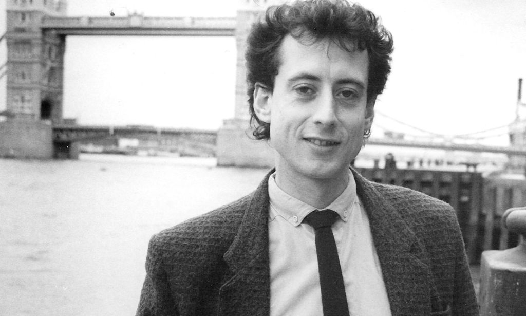 Peter Tatchell in a photograph promoting his candidacy in the 1983 Bermondsey by-election. He is pictured by a bridge wearing a suit in a black and white shot.