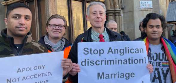 Photo of protestors standing outside the Church of England's General Synod holding signs. One of them reads "Stop Anglican discrimination. Marriage equality now".