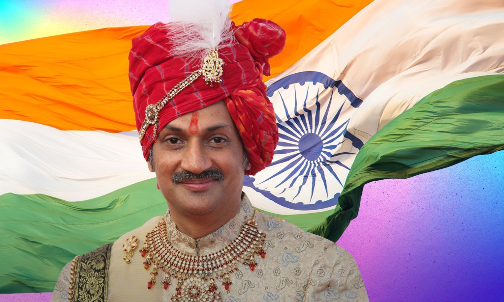 Prince Manvendra Singh Gohil, a smiling man wearing a gold top, red jewelled necklace and red turban with a feather.