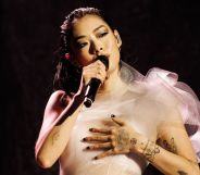 Rina Sawayama performs in a white dress while holding a black microphone.
