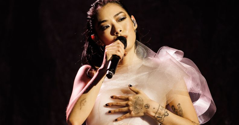Rina Sawayama performs in a white dress while holding a black microphone.