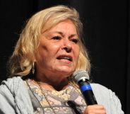 Roseanne barr wearing a patterned top and grey cardigan holding a black and blue microphone.