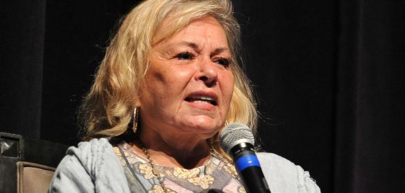 Roseanne barr wearing a patterned top and grey cardigan holding a black and blue microphone.