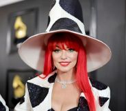 Shania Twain at the 2023 Grammy red carpet with red hair and a cow-print suit and oversized top hat.