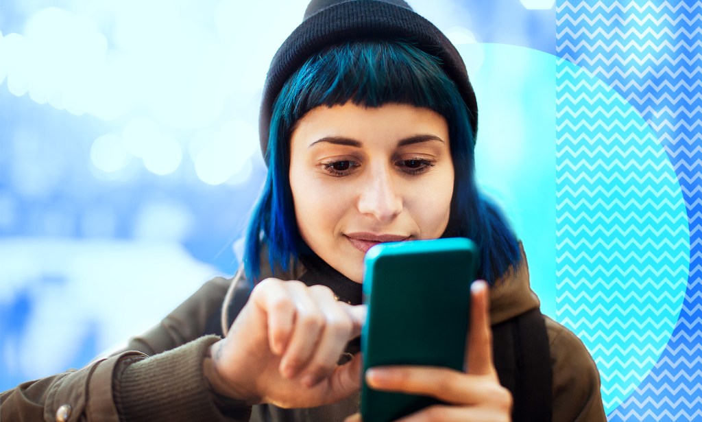 A woman with blue hair and a beanie is looking at her phone.
