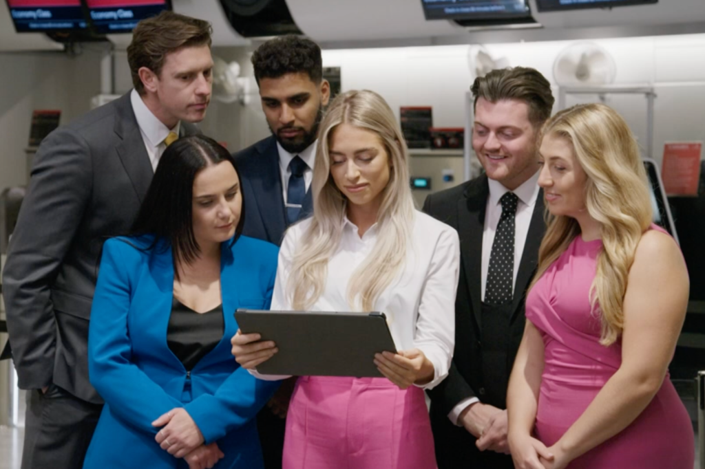 Candidates on The Apprentice crowd around an iPad