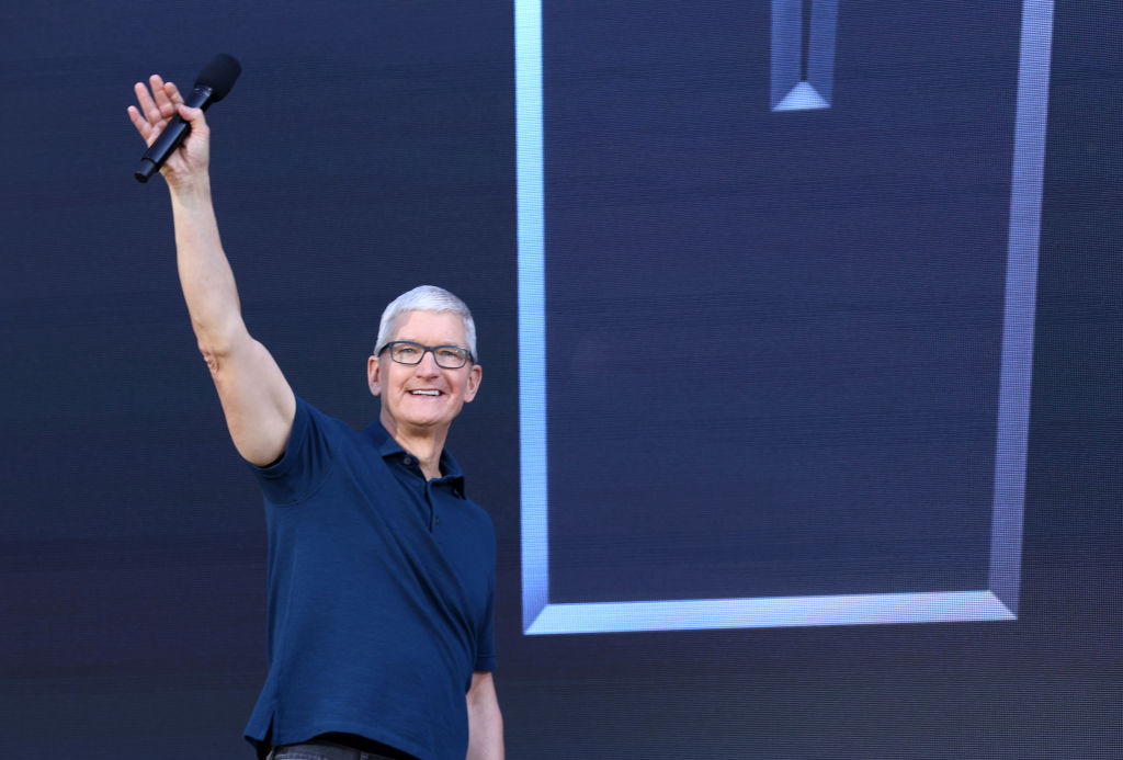 Tim Cook of Apple Inc is smiling and waving to a crowd while speaking on stage.