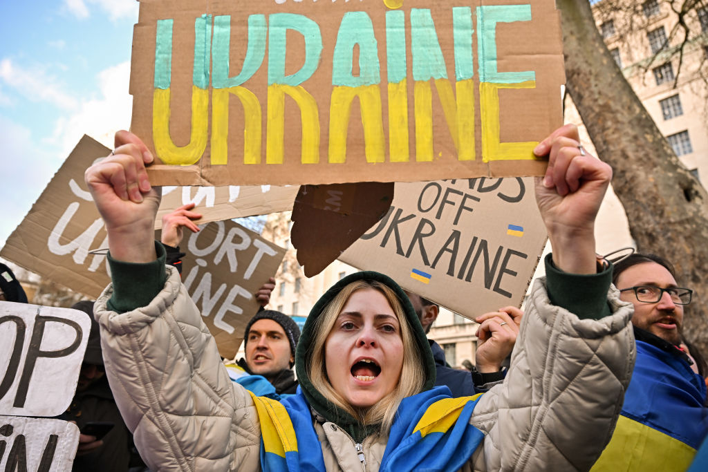 Ukrainians demonstrate outside Downing Street against Russia's invasion of Ukraine. A woman is pictured holding up a sign which says "Ukraine" in blue and yellow writing. She is wearing a scarf in the Ukrainian colours around her neck.
