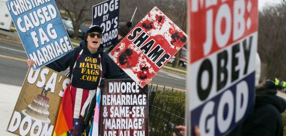 A member of the Westboro Baptist Church holding up various hateful signs.