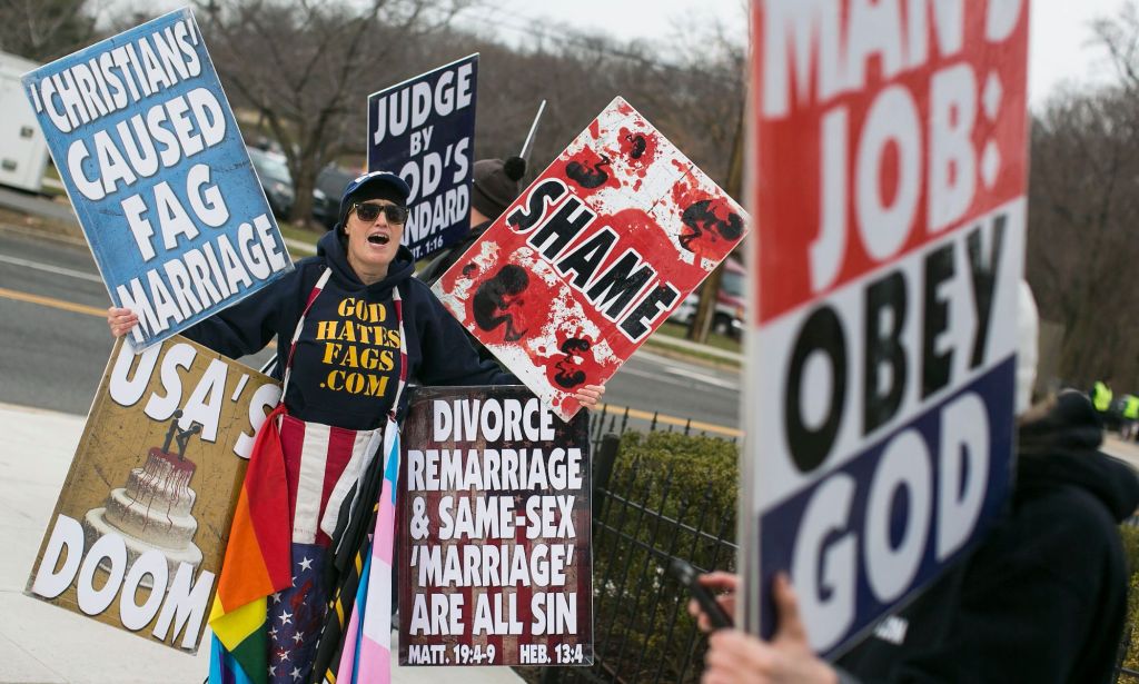 A member of the Westboro Baptist Church holding up various hateful signs.