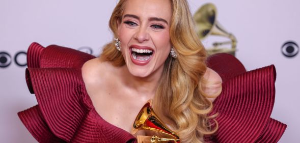 Adele wears a red dress as she laughs and holds a golden award after the Grammys