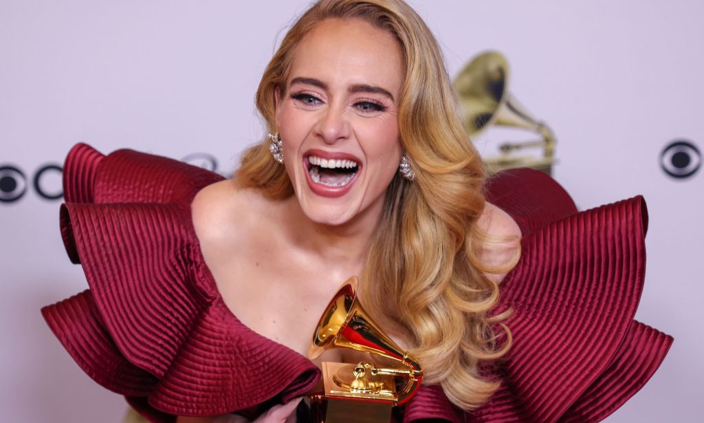 Adele wears a red dress as she laughs and holds a golden award after the Grammys