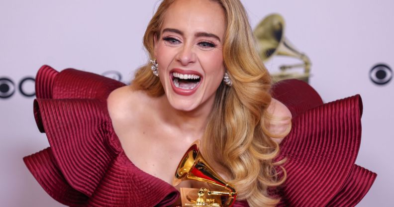 Adele wears a red dress as she laughs and holds a golden award after the Grammys