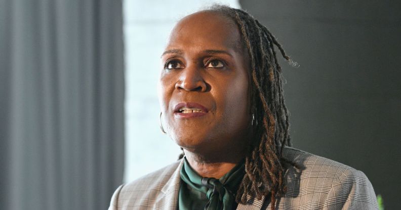 Andrea Jenkins sits infront of a curtained window, wearing red lipstick and her hair in locks, smiling