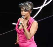 Ariana DeBose wearing a pink satin jumpsuit, holding a microphone