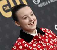 Photo of actor Bella Ramsey wearing a red and white floral-pattern shirt smiling at a press event