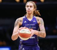 Brittney Griner wears a purple Phoenix Mercury basketball uniform as she holds a white and orange basketball in her hands