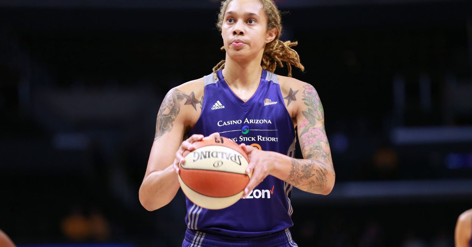 Brittney Griner wears a purple Phoenix Mercury basketball uniform as she holds a white and orange basketball in her hands
