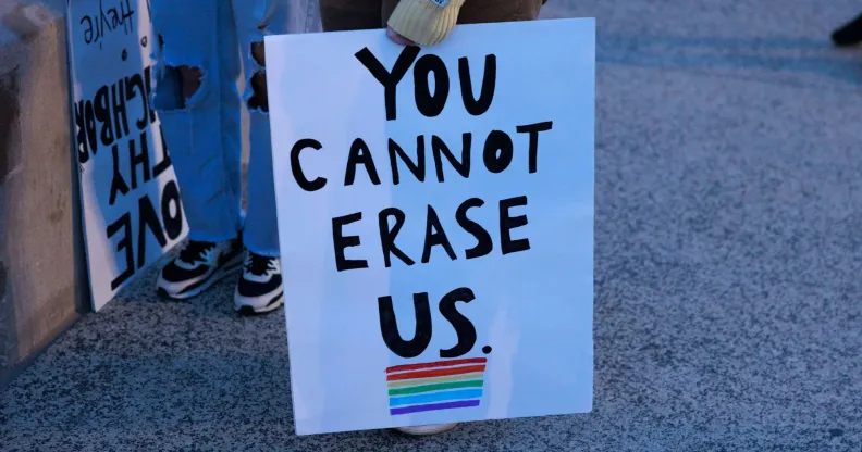 A person holds a sign reading 'You cannot erase us' with a rainbow LGBTQ+ flag below it during a protest against Republish's pushing 'Don't Say Gay or Trans' bills