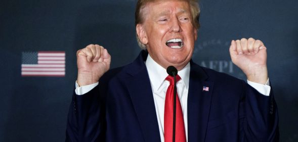 Republican president Donald Trump wears a suit and tie as he holds both his hands up near his head in the shape of fists