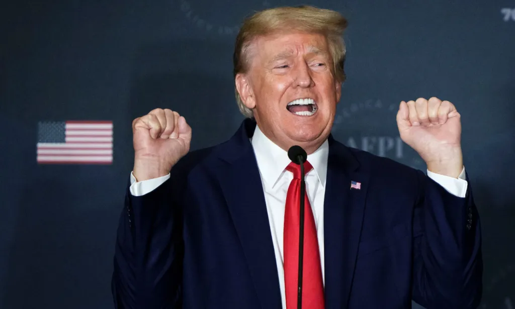 Republican president Donald Trump wears a suit and tie as he holds both his hands up near his head in the shape of fists