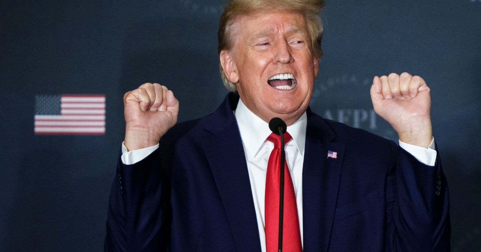 Republican president Donald Trump wears a suit and tie as he holds both his hands up near his head in the shape of fists