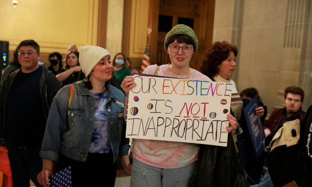 A person holds up a sign reading 'Our existence is not inappropriate' with varying LGBTQ+ Pride flag colours at a protest against Republicans pushing 'Don't Say Gay or Trans' bills