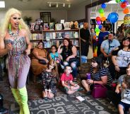 A drag queen wearing a sparking outfit dances while performing before a young audience at a reading event