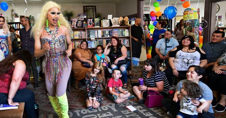 A drag queen wearing a sparking outfit dances while performing before a young audience at a reading event