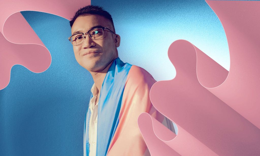 Henry Edward Tse wears a trans Pride flag draped across his shoulders with a blue background and pink curved designs in the corner of the graphic