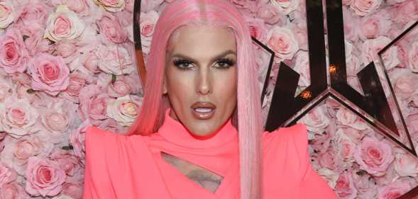 Photo of makeup artist Jeffree Star wearing a pink dress and pink wig standing in front of a background of pink roses