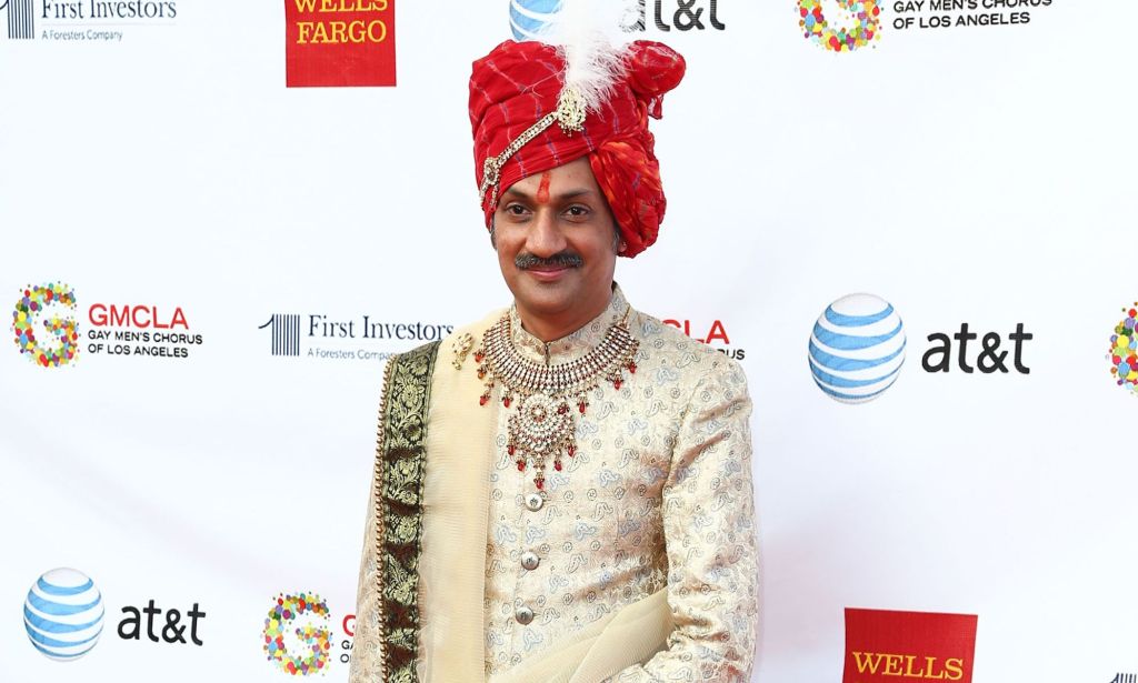 Indian Prince Manvendra Singh Gohil wears a red head covering with a white flower, and he has a white outfit with elaborate embroidery