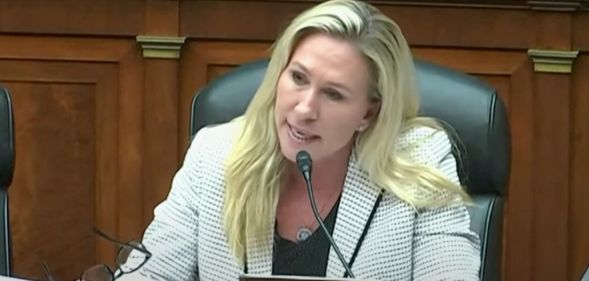 Marjorie Taylor Greene wears a black top and white patterned blazer as she sits at a House committee hearing
