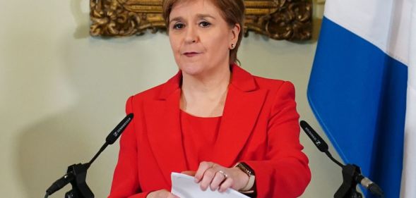 Nicola Sturgeon in a red suit speaking at a lecturn