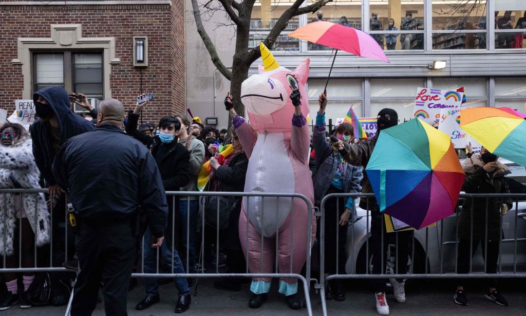 A crowd of people, including one person wearing an inflatable pink unicorn costume, show up to block out hateful protestors at a drag event